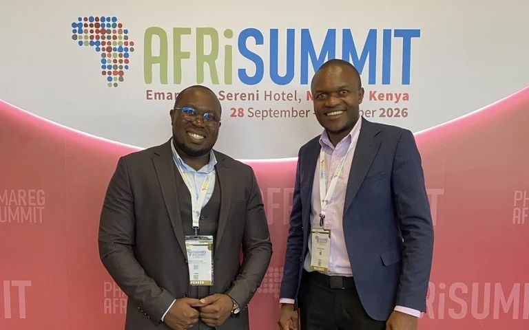 Two men wearing conference badges pose in front of an AfriSummit backdrop