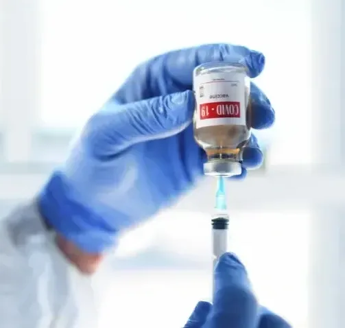 A gloved hand drawing a COVID-19 vaccine from a vial into a syringe