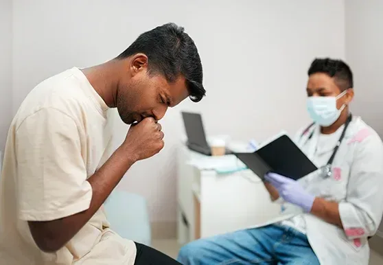 A patient coughing during a consultation while a masked doctor takes notes