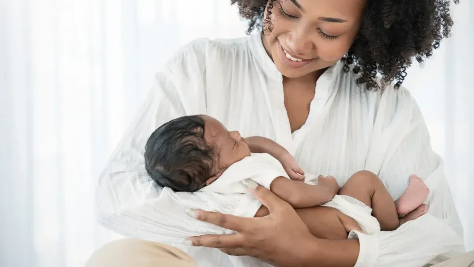 A mother in a white shirt smiling down at the newborn she holds in her arms