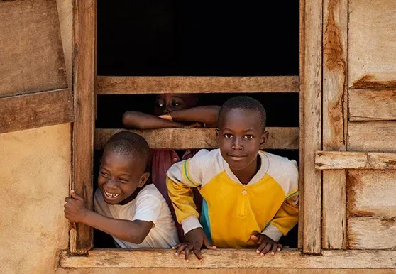 Two children smiling out of a wooden window frame